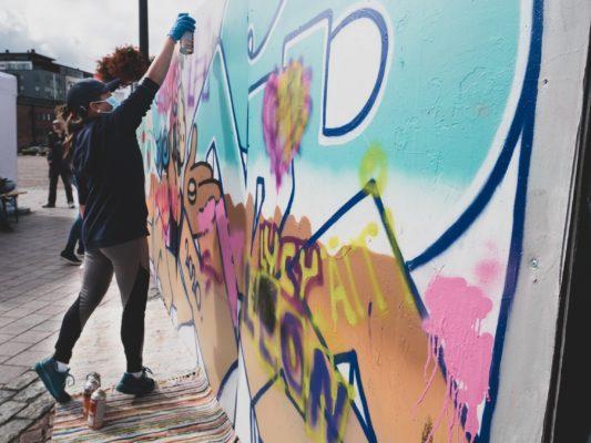 Nuori nainen maalaa spraymaalilla graffittia.
